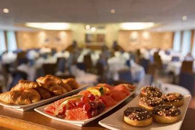Seine Comtesse Thurgau Flusskreuzfahrt-uffet Ein Buffet auf dem Flusskreuzfahrtschiff Seine Comtesse von Thurgau Reisen, das eine Auswahl an frischen Croissants, Obst und Donuts präsentiert. Im Hintergrund sind die elegant gedeckten Tische des Essbereichs sichtbar, die eine einladende Atmosphäre schaffen.