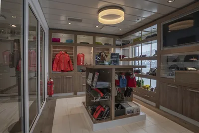Flusskreuzfahrten-boutique ocean albatros Die Boutique auf dem Flusskreuzfahrtschiff Ocean Albatros von Thurgau Reisen, die eine Auswahl an Kleidung und Accessoires anbietet. Regale aus Holz präsentieren farbenfrohe Jacken und Souvenirs, während eine moderne Beleuchtung dem Raum eine einladende Atmosphäre verleiht.
