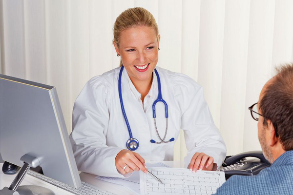 Flusskreuzfahrt Schiffsarzt Thurgau Ein Schiffsarzt in einem modernen Büro spricht freundlich mit einem Patienten. Die Ärztin trägt einen weißen Kittel und ein Stethoskop. Im Hintergrund ist ein Computer zu sehen, was die medizinische Umgebung an Bord eines Flusskreuzfahrtschiffs von Thurgau Reisen verdeutlicht.