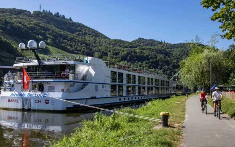 Antonio Bellucci an Anlegestelle Kreuzfahrtschiff Thurgau Reisen Antonio Bellucci, das an einer Anlegestelle vertäut wurde. Daneben ist ein Fußweg und bewaldete Berge zu sehen