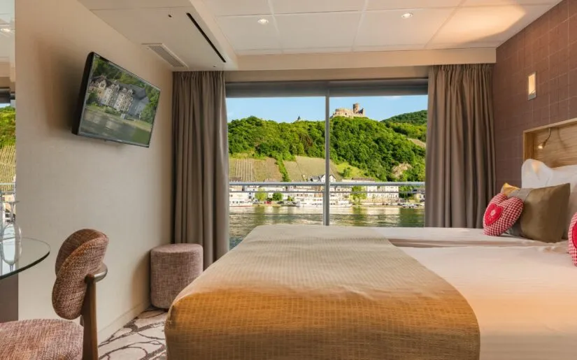 Edelweiss gemütliche Kabine Kabine der MS Edelweiss mit Panoramafenster und französischem Balkon mit Ausblick auf Stadt am Flussufer.