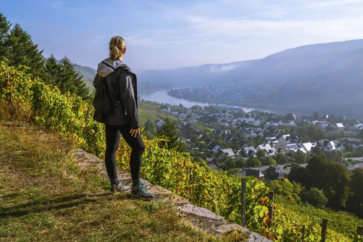 Wanderin genießt den Sonnenaufgang über einer kleinen europäischen Stadt Winningen, Deutschland mit Weinbergen im Rheintal