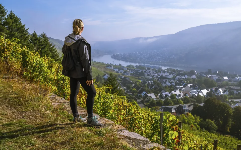 Wanderin genießt den Sonnenaufgang über einer kleinen europäischen Stadt Winningen, Deutschland mit Weinbergen im Rheintal