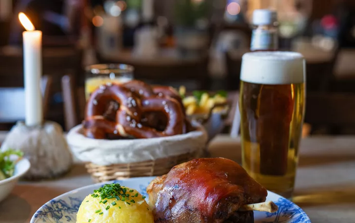 © NIKIBA - stock.adobe.com - Traditionelle Schweinshaxe mit Knödel und Bier im gemütlichen Wirtshaus